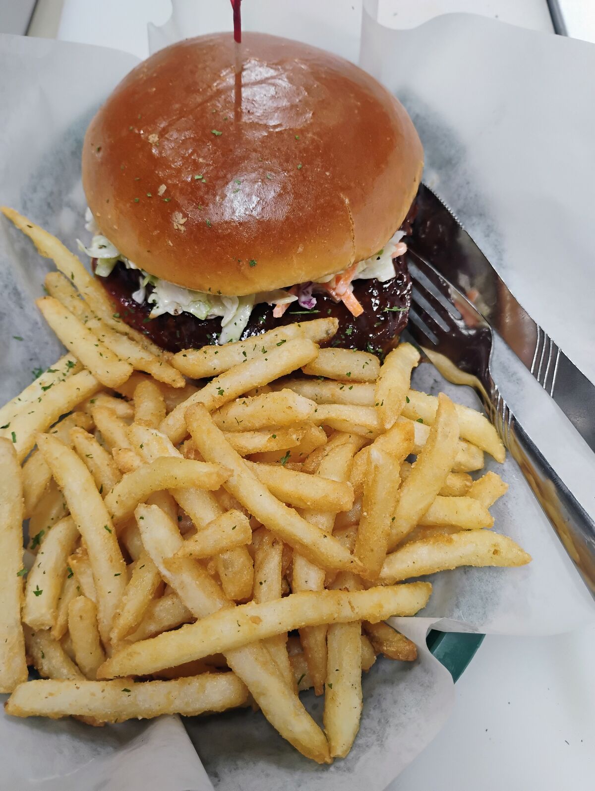 BBQ slaw burger on a brioche bun topped with coleslaw and BBQ sauce, served with a generous portion of seasoned fries