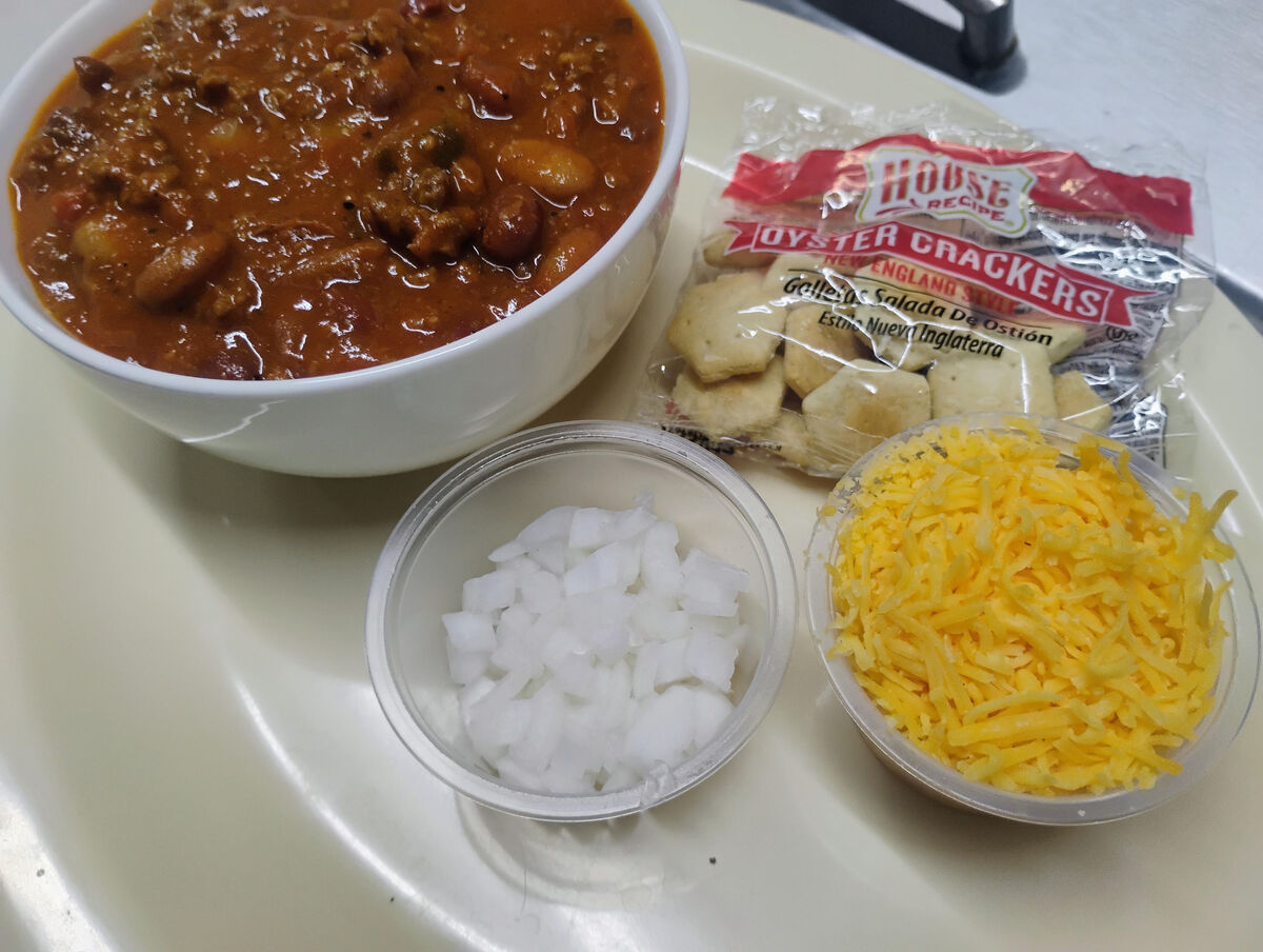 Hearty bowl of Whalen's chili served with oyster crackers, diced onions, and shredded cheddar